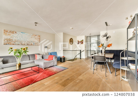 A stylish modern living room featuring a cozy sofa, elegant decor, and a dining area. The warm color palette and natural light create an inviting atmosphere. 124807038