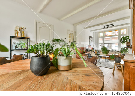 A contemporary interior scene featuring a round wooden table adorned with potted plants, illuminated by natural light, creating a warm and inviting atmosphere. 124807043
