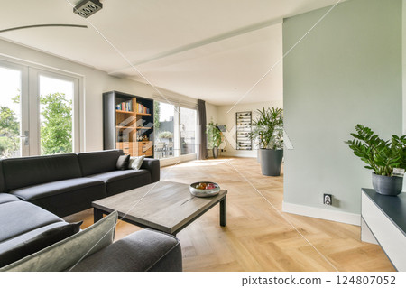A contemporary living room featuring a cozy couch, wooden flooring, and greenery, creating an inviting and stylish atmosphere for relaxation. 124807052