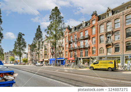 A picturesque urban scene featuring beautiful trees lining a street with classic architecture and vibrant storefronts. The atmosphere is lively and inviting. 124807271