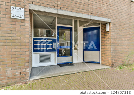 A contemporary entrance featuring blue doors and a brick facade, set in an urban environment with greenery visible. Ideal for architectural inspiration. 124807318