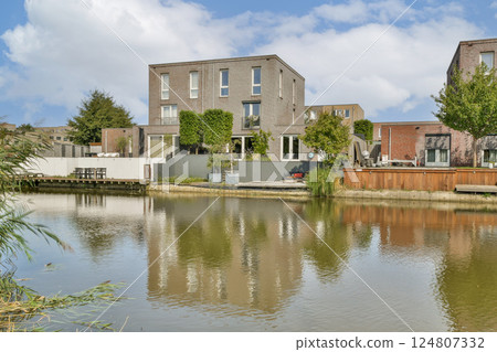 A contemporary residential structure surrounded by greenery and reflected in a tranquil waterbody, showcasing modern architectural design. 124807332