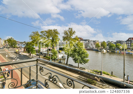 This image showcases a picturesque urban landscape featuring a waterway bordered by lush trees, under a clear blue sky. It merges nature and architecture beautifully. 124807336