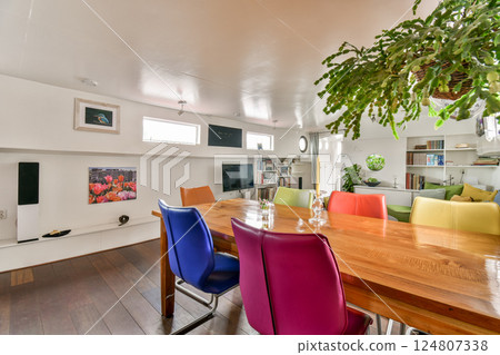 A stylish and inviting modern living space featuring colorful chairs, plants, and natural light enhancing the vibrant atmosphere. A stylish and inviting modern living space featuring colorful chairs, plants, and natural light enhancing the vibrant atmosphere. 124807338