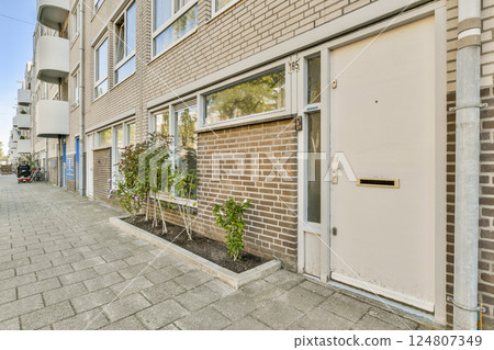 A contemporary building entrance featuring a beige door, large windows, and neatly arranged plant beds, capturing the essence of urban living. 124807349