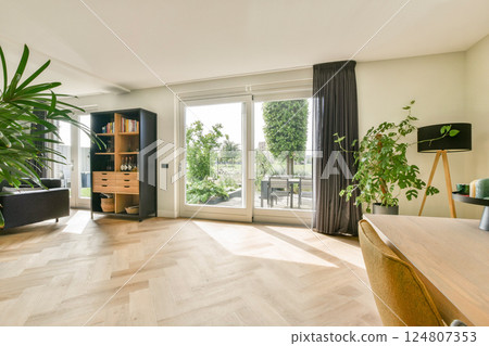 A contemporary living room featuring large windows, stylish furniture, and vibrant indoor plants, creating a bright and welcoming atmosphere. 124807353