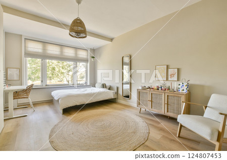 A bright and airy bedroom featuring a cozy bed, natural light from large windows, and minimalist decor for a tranquil atmosphere. 124807453