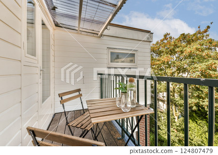 A stylish balcony featuring wooden furniture and a decorative plant. The setting is bright and airy, perfect for relaxation and enjoying nature. A stylish balcony featuring wooden furniture and a decorative plant. The setting is bright and airy, perfect for relaxation and enjoying nature. 124807479
