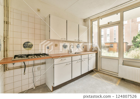 A minimalistic kitchen featuring white cabinets, a gas stove, and large windows allowing plenty of natural light, creating an inviting atmosphere. A minimalistic kitchen featuring white cabinets, a gas stove, and large windows allowing plenty of natural light, creating an inviting atmosphere. 124807526
