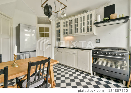 A stylish modern kitchen featuring a black and white checkered floor, sleek cabinetry, and a minimalist design with elegant lighting and decor. A stylish modern kitchen featuring a black and white checkered floor, sleek cabinetry, and a minimalist design with elegant lighting and decor. 124807550
