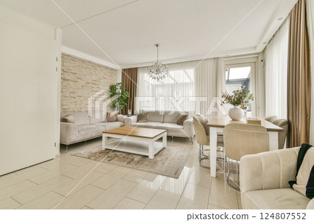 A chic and spacious modern living room featuring elegant furniture, large windows, and stylish decor, creating a welcoming and comfortable atmosphere. 124807552