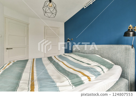 Elegant modern bedroom featuring a cozy bed with striped bedding, minimalist decor, and a stylish light fixture, creating a serene atmosphere. 124807553