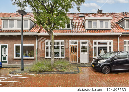 An inviting urban house showcases a blend of architectural styles with a well-maintained exterior, colorful foliage, and a parked car nearby. An inviting urban house showcases a blend of architectural styles with a well-maintained exterior, colorful foliage, and a parked car nearby. 124807583