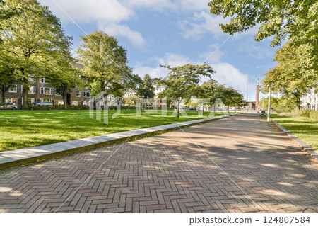 A serene pathway winding through a lush city park, framed by vibrant trees and modern buildings, inviting visitors to enjoy nature and relaxation. A serene pathway winding through a lush city park, framed by vibrant trees and modern buildings, inviting visitors to enjoy nature and relaxation. 124807584