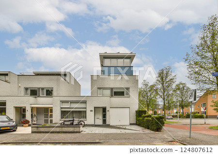 A contemporary urban residence featuring sleek lines and unique design elements, complemented by surrounding greenery and a clear blue sky. 124807612