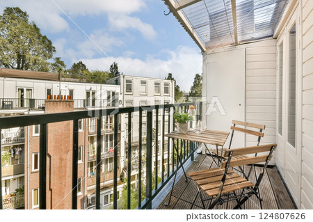 A serene view from a cozy apartment balcony overlooking buildings and greenery, showcasing modern architecture and a peaceful atmosphere. 124807626