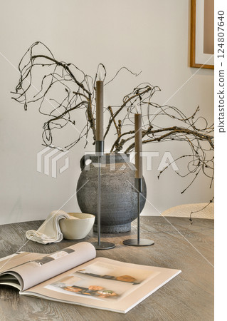A sophisticated table setting featuring minimalist decor, including a unique vase, candles, and a stylish book, exuding contemporary charm. A sophisticated table setting featuring minimalist decor, including a unique vase, candles, and a stylish book, exuding contemporary charm. 124807640