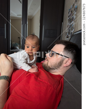 Man in Red Shirt Holding Baby on Bed 124807673