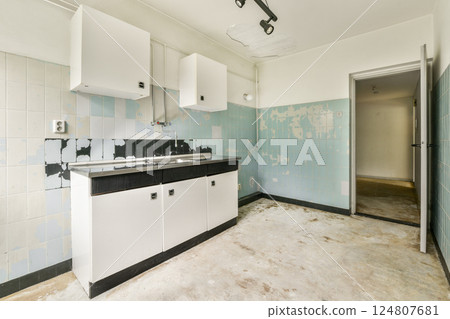 An abandoned kitchen showcasing peeling paint and faded blue tiles, with minimal fixtures left. The space exudes a sense of neglect and disrepair. An abandoned kitchen showcasing peeling paint and faded blue tiles, with minimal fixtures left. The space exudes a sense of neglect and disrepair. 124807681