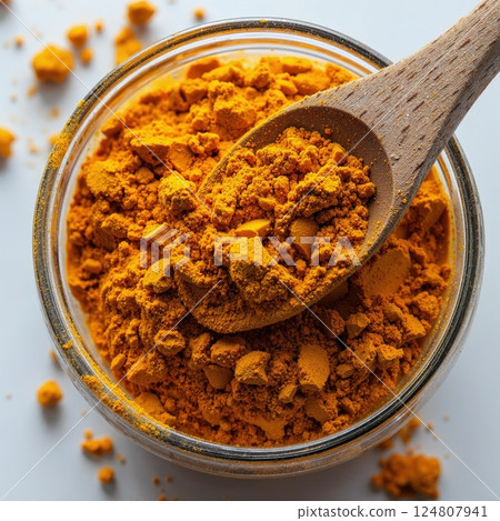 Bright organic turmeric spice in rustic wooden spoon and glass jar for culinary and health uses 124807941