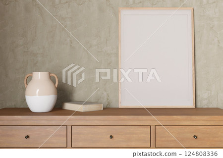 A minimalist interior showcases an empty picture frame on a wooden console, accompanied by a decorative vase and book. This setup invites personal artistic expression and creativity. 3D render. 124808336