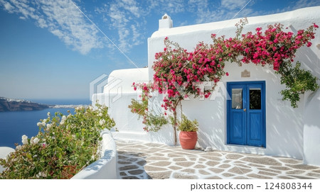 A whitewashed house with a vibrant blue door and cascading bougainvillea overlooks the serene Aegean Sea under a bright blue sky 124808344