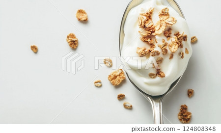 A spoonful of creamy yogurt topped with crunchy cereal flakes is beautifully arranged on a minimal light background 124808348