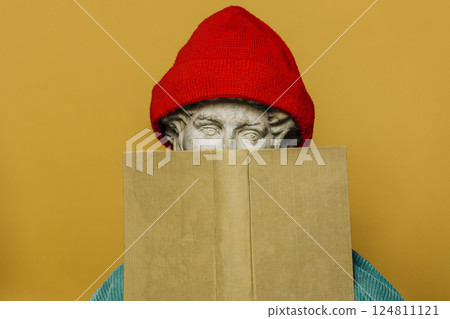 Antique statue of a young man in a red hipster hat hiding behind a book 124811121