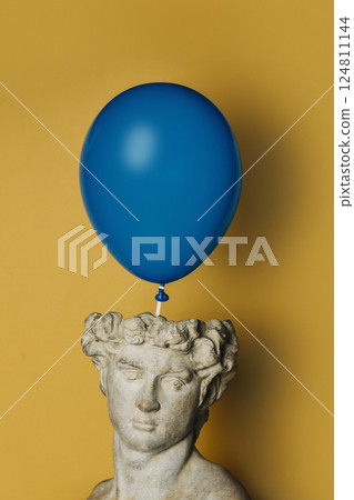antique statue of a young man on a yellow background with a blue balloon 124811144