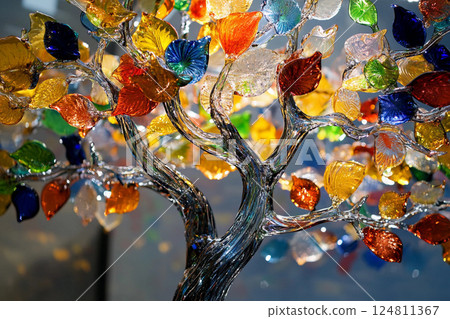 Colorful glass tree sculpture shines against a bright blue sky with white clouds during daylight hours 124811367
