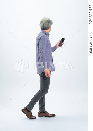 Full-body photo of a senior man walking with a smartphone Full-body photo of a senior man walking with a smartphone 124811482