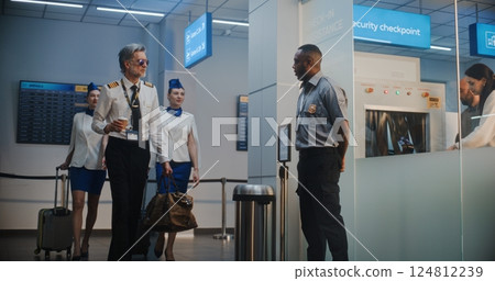 Airport Terminal: Airline Pilot and Two Flight Attendants Walking, Passing by Security Officer 124812239