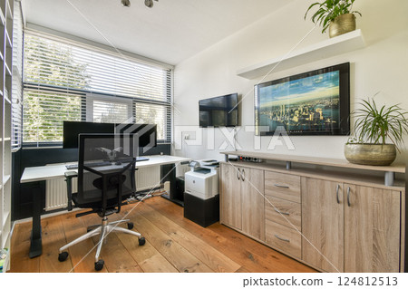 A sleek home office featuring a stylish desk, multiple monitors, wooden flooring, and contemporary decor, creating a productive environment. 124812513