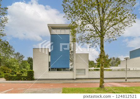 A striking modern building showcasing a blue facade amidst lush greenery and clear skies. The design emphasizes clean lines and contemporary aesthetics. 124812521