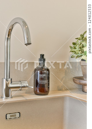 A sleek bathroom sink with a polished faucet and a stylish amber bottle of hand wash, accompanied by greenery on a wooden tray to enhance the decor. A sleek bathroom sink with a polished faucet and a stylish amber bottle of hand wash, accompanied by greenery on a wooden tray to enhance the decor. 124812533