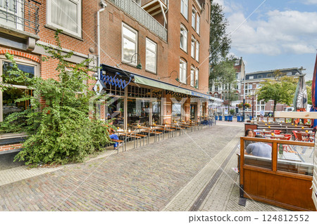 A picturesque cafe situated on a cobbled street, showcasing outdoor seating and vibrant trees, ideal for relaxation and socializing in an urban setting. 124812552