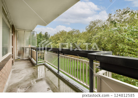 A modern balcony overlooks a lush green landscape, offering an inviting space for relaxation and enjoyment of nature's beauty. 124812585