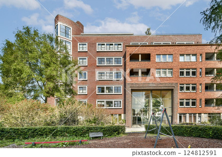 Contemporary architecture featuring a red-brick facade, large windows, and landscaped surroundings, enhancing urban living's aesthetic and functional appeal. 124812591