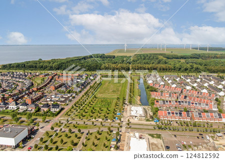Expansive aerial view showcasing a blend of residential neighborhoods and green spaces adjacent to a body of water, featuring wind turbines in the background. Expansive aerial view showcasing a blend of residential neighborhoods and green spaces adjacent to a body of water, featuring wind turbines in the background. 124812592