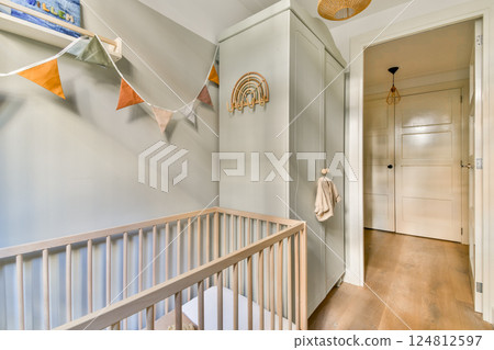 A beautifully designed baby nursery featuring a modern crib, storage cabinet, and colorful bunting. The soothing atmosphere is perfect for any infant. A beautifully designed baby nursery featuring a modern crib, storage cabinet, and colorful bunting. The soothing atmosphere is perfect for any infant. 124812597
