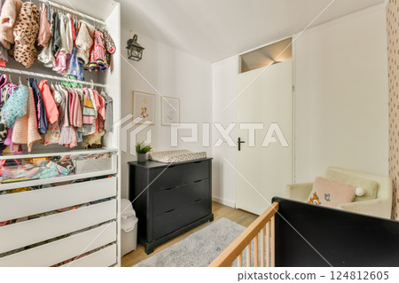 A bright and inviting nursery space featuring a colorful clothing rack, a sleek dresser, and a cozy sleeping area. Perfect for creating a nurturing environment. 124812605