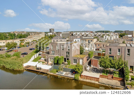 Aerial view showcasing contemporary houses beside a tranquil waterway, enhanced by lush greenery and clear blue skies, exemplifying urban living in harmony with nature. 124812606