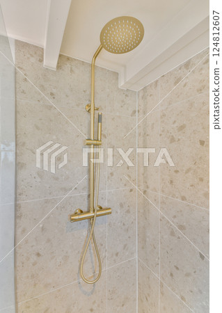 A luxurious gold shower head mounted on a stylish marble wall, showcasing contemporary bathroom design with sleek lines and an appealing color scheme. 124812607