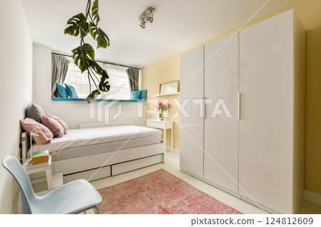 A chic and cozy bedroom featuring a minimalist design with soft colors, a stylish bed, white furniture, and a decorative rug that adds warmth to the space. 124812609