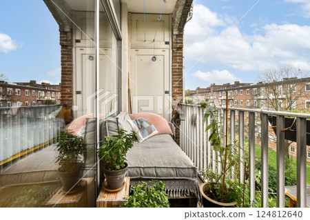 A cozy balcony featuring a cushioned seating area adorned with plants and a view reflecting a vibrant urban landscape. A cozy balcony featuring a cushioned seating area adorned with plants and a view reflecting a vibrant urban landscape. 124812640