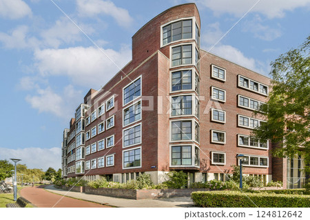 This striking modern apartment building features a unique architectural design, large windows, and a beautiful surrounding landscape, enhancing urban living aesthetics. This striking modern apartment building features a unique architectural design, large windows, and a beautiful surrounding landscape, enhancing urban living aesthetics. 124812642