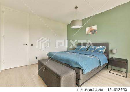 A stylish modern bedroom featuring a cozy bed dressed in blue linens, a minimalist design, and calming green wall accents, perfect for relaxation. A stylish modern bedroom featuring a cozy bed dressed in blue linens, a minimalist design, and calming green wall accents, perfect for relaxation. 124812760