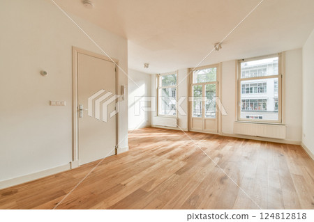 A spacious, well-lit room featuring large windows that bring in natural light, complemented by warm wooden flooring and minimalist design. Ideal for various uses. 124812818