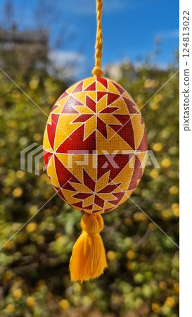 Beautiful Ukrainian pysanka representing traditional Easter eggs with vibrant patterns in red and yellow hanging against a floral background during spring season celebrations Beautiful Ukrainian pysanka representing traditional Easter eggs with vibrant patterns in red and yellow hanging against a floral background during spring season celebrations 124813022