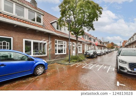 A picturesque street scene showcasing charming buildings lined with vibrant greenery and parked cars, all under a soft, rainy sky. A picturesque street scene showcasing charming buildings lined with vibrant greenery and parked cars, all under a soft, rainy sky. 124813028